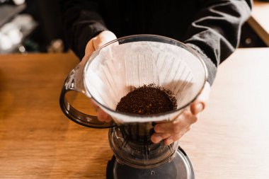 Barista, çaydanlıktan su dökmeden önce kağıt filtrede öğütülmüş kahveyle akıllı kahve damlatıcısının üzerine döküyor. Kafedeki akıllı kahve damlatıcısının üzerine dökme işlemi