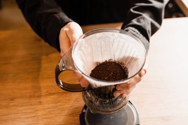 Barista, çaydanlıktan su dökmeden önce kağıt filtrede öğütülmüş kahveyle akıllı kahve damlatıcısının üzerine döküyor. Kafedeki akıllı kahve damlatıcısının üzerine dökme işlemi