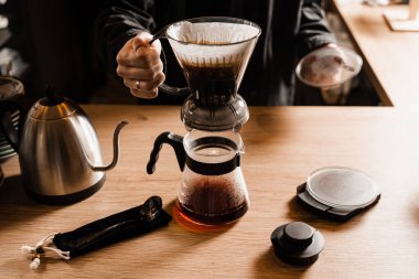 Kafedeki ahşap masaya filtre ve aksesuarların üzerine dökülen akıllı kahve damlası. Damlatma filtresi kahvesi demleniyor. Zeki kahve damlası evde filtre kahve yapmak için alternatif bir yöntem.