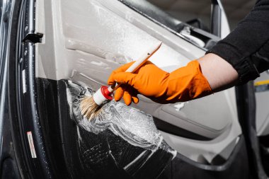 Araba temizleme servisi. Temizlik işçisi, müşterilerin iç çamaşırlarını yıkıyor. Araba kapısı paneliyle köpük ve deterjan temizleme işlemi