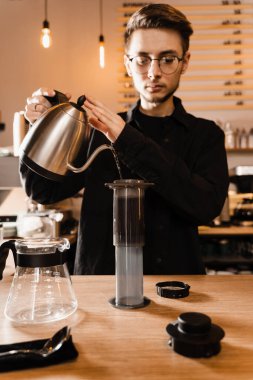 Barista bir çaydanlıktan diğerine sıcak su döküyor. Bira üreten uçaklar. Kavrulmuş sıcak su dökülüyor ve kahve çekirdekleri uçakla eziliyor.