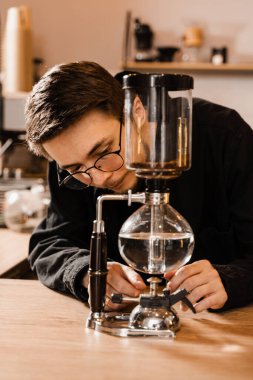 Barista alternatif kahve demlemek için sifon cihazında su kaynatıyor. Kahve ile kaynar suyu karıştırmak için elektrikli süpürge.