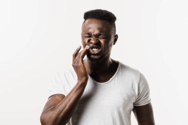 Beyaz arka planda Afrikalı bir adamın diş ağrısı. Afrikalı Amerikalılar yanaklarına dokunuyor ve beyaz arka planda dişlerinin ağrıdığını hissediyorlar. Diş çürüğü, enfeksiyon ya da diş eti yaralanması.
