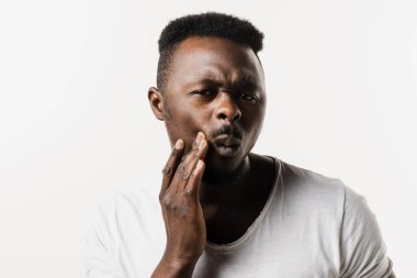 Afrikalı Amerikalı adam yanağına dokunuyor ve diş ağrısı ve diş rahatsızlığı çekiyor. Diş çürüğü, enfeksiyon ya da diş eti yaralanması olan Afrikalı bir adam.