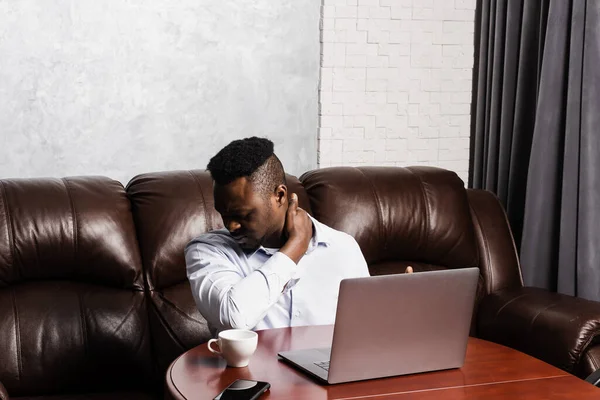 stock image African man with laptop feel neck and spine pain because of spinal nerves compression. Cervical spine osteochondrosis is radicular syndromes after long work at the computer