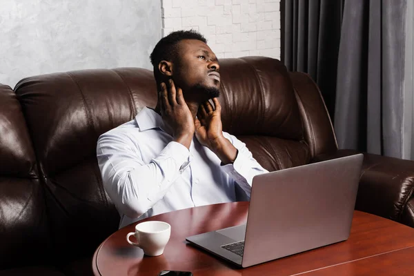 African man feels neck pain after working for long hours with laptop online in office. Cervical spine osteochondrosis is radicular syndromes of african american man