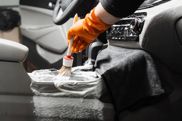 Dry cleaning with brush of gearbox and dashboard in car. Auto detailing service. Cleaning individual elements of interior in auto