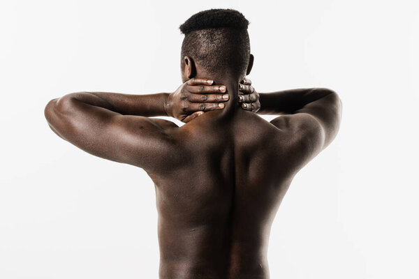 Muscular shirtless african man feel spine and neck pain because of spinal nerves compression on white background. Cervical spine osteochondrosis is radicular syndromes of african american man