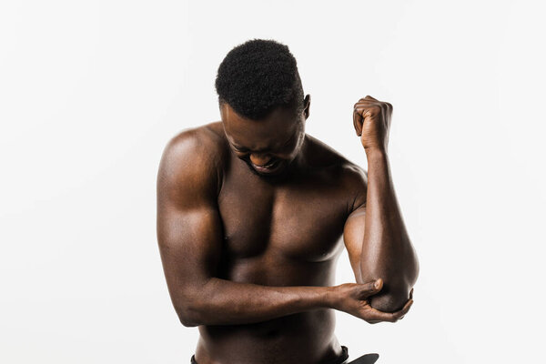 Sport traumatology. Elbow injury of muscular african american man on white background. African american man with pain and bruise in his arm due to an accident