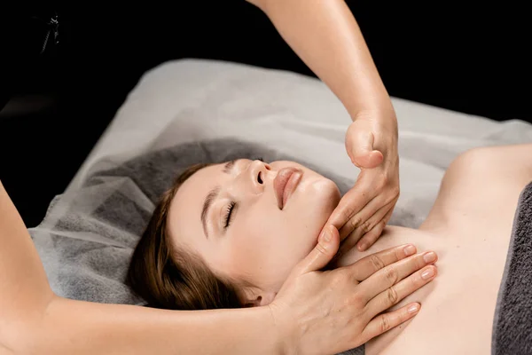 stock image Girl with closed eyes is relaxing on face and neck massage in spa. Masseur is making facial massage for young woman in spa. Facebuilding and relaxing procedures