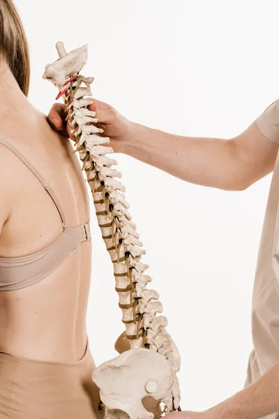 Orthopedist showing spinal column model with girl on white background. Scoliosis is sideways curvature of the spine. Backbone anatomical model with young woman