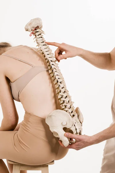 Orthopedist showing spinal column model with girl on white background. Scoliosis is sideways curvature of the spine. Backbone anatomical model with young woman