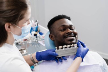 Diş macunları ya da implantlar diş sağlığı kliniğindeki Afrikalı hastalar için diş beyazlatma için uygun renk örnekleri. Diş rengi gölgeler yakın çekim rehberidir. Afrikalı diş hekimi
