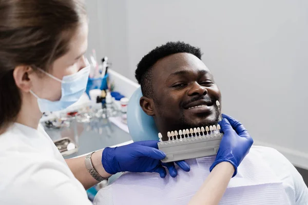 Veneers or implants teeth color matching samples for tooth whitening for african patient in dental clinic. Teeth color shades guide close-up. African man in dentistry