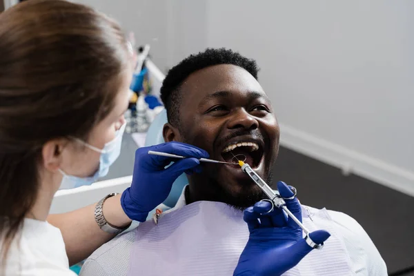 Dentist injects anesthesia syringe of the diseased teeth for the african man patient. Caries treatment