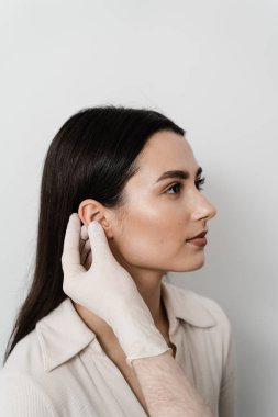 Doktor otoplasti estetik ameliyatından önce kızın kulağını muayene ediyor. Otoplasti, pinnanın cerrahi olarak yeniden şekillendirilmesi, ya da düzensizliği düzeltmek ve görüntüyü iyileştirmek için dış kulak.