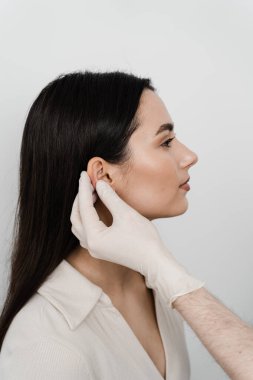 Doktor otoplasti estetik ameliyatından önce kızın kulağını muayene ediyor. Otoplasti, pinnanın cerrahi olarak yeniden şekillendirilmesi, ya da düzensizliği düzeltmek ve görüntüyü iyileştirmek için dış kulak.