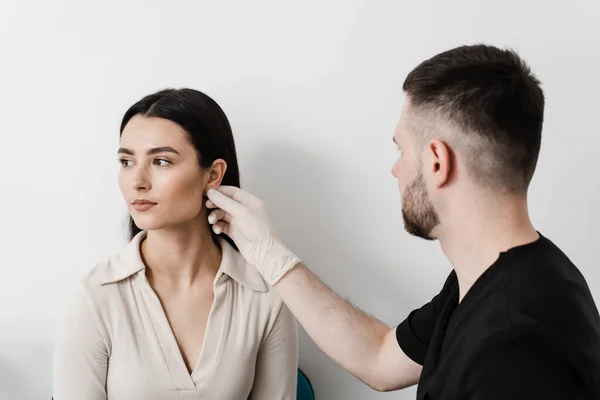 Stock image Otoplasty is surgical reshaping of the pinna, or outer ear for correcting an irregularity and improving appearance. Surgeon doctor examines girl ear before otoplasty cosmetic surgery