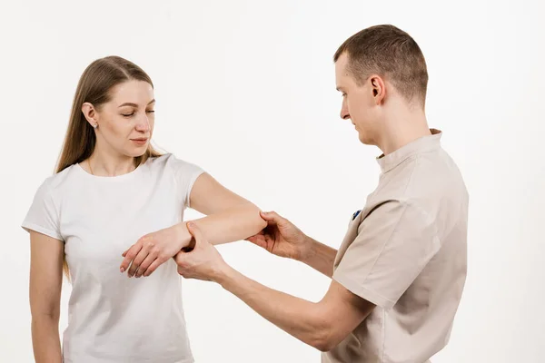 Tennis elbow, or lateral epicondylitis is painful condition of the elbow joint caused by overuse. Orthopedist traumatologist examines elbow joint with pain and prescribes treatment for girl patient