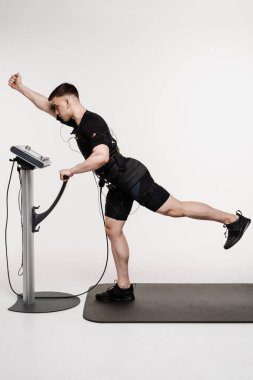 Kas yapısı olan erkek sporcu, kasları çalıştırmak için elektirikli impulslar uygulayan EMS giysisiyle egzersiz yapar. Antrenör spor antrenmanı için elektrik kas stimülasyonu kıyafeti kullanıyor.