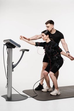 EMC grup eğitimi. Eğitmen, EMC kostümlü bir kızı fiziksel egzersiz yaparken gösteriyor. Elektrik kas stimülasyonu için spor grubu eğitimi