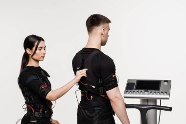 Kadın ve erkek, beyaz arka plandaki kasları canlandırmak için elektriksel impulslar kullanan EMS giysisinin kontağı. Elektrik kas stimülasyonu için spor grubu eğitimi