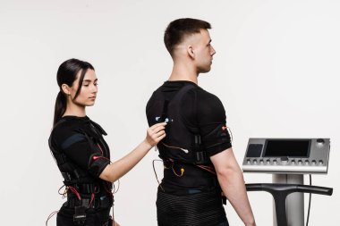 Kadın ve erkek, beyaz arka plandaki kasları canlandırmak için elektriksel impulslar kullanan EMS giysisinin kontağı. Elektrik kas stimülasyonu için spor grubu eğitimi