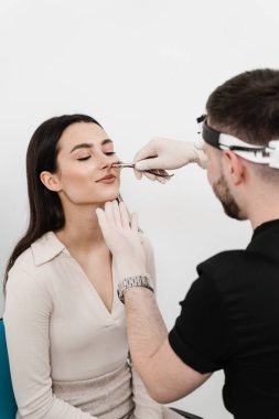 Otolaryngologist examines girl nose before procedure of endoscopy of nose. Consultation with ENT doctor. Rhinoscopy of woman nose