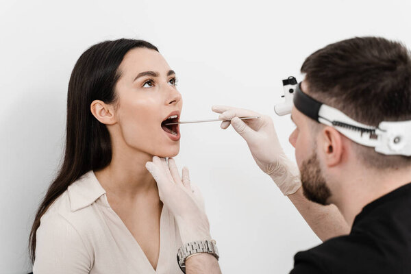 ENT doctor examines woman throat with spatula. Consultation with otolaryngologist. Girl opens her mouth and ENT doctor examines the sore throat