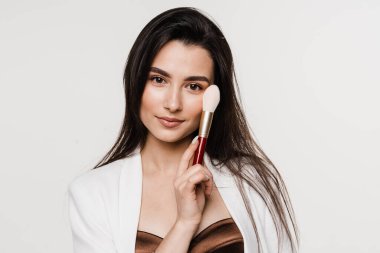 Beyaz arka planda makyaj köpüğü olan profesyonel bir makyöz. Çekici kız elinde far fırçalar ve gülümsüyor.