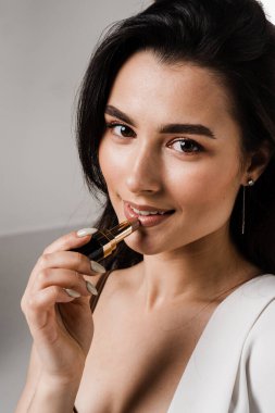 Makyöz kız dudaklarını beyaz arka planda rujla boyuyor. Çekici model dudaklarına mat pastel ruj sürüyor.