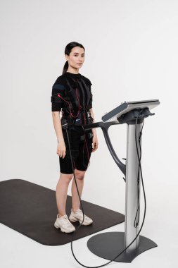 Beyaz arka planda EMS kıyafetli kız. Elektrik kas stimülasyonu giysisinde spor eğitimi