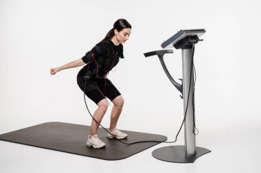 EMS Elektrik Kas Uyarma Kıyafeti 'nde spor eğitimi. Sağlık görevlisi kız, beyaz arka plandaki kasları canlandırmak için elektriksel impulslar kullanan spor eğitimi yapıyor.