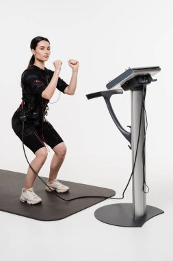 Formda kız, beyaz arka plandaki kasları uyarmak için elektriksel impulsları kullanan EMS giysisiyle fiziksel egzersiz yapıyor. Elektrik kas stimülasyonu giysisinde spor eğitimi