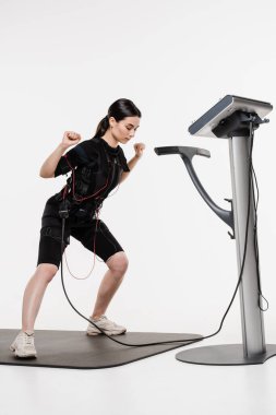 Sportif kız EMS giysisiyle egzersiz yapıyor, kasları çalıştırmak için elektriksel impulslar uyguluyor. Genç bayan antrenör spor antrenmanı yapıyor EMS elektrik kas stimülasyonu elbisesi kullanıyor.