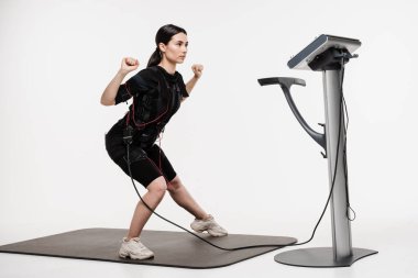 Sportif kız EMS giysisiyle egzersiz yapıyor, kasları çalıştırmak için elektriksel impulslar uyguluyor. Genç bayan antrenör spor antrenmanı yapıyor EMS elektrik kas stimülasyonu elbisesi kullanıyor.