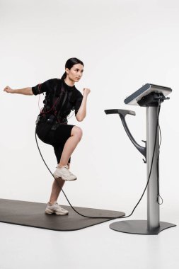 Sportif kız EMS giysisiyle egzersiz yapıyor, kasları çalıştırmak için elektriksel impulslar uyguluyor. Genç bayan antrenör spor antrenmanı yapıyor EMS elektrik kas stimülasyonu elbisesi kullanıyor.