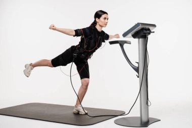 Genç bayan antrenör EMS elektrik kas stimülasyonu kıyafeti kullanarak spor antrenmanı yapıyor. Sportif kız EMS giysisiyle egzersiz yapıyor, kasları çalıştırmak için elektriksel impulslar uyguluyor.