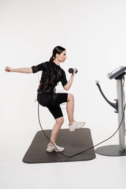 Genç bayan antrenör EMS elektrik kas stimülasyonu kıyafeti kullanarak spor antrenmanı yapıyor. Sportif kız EMS giysisiyle egzersiz yapıyor, kasları çalıştırmak için elektriksel impulslar uyguluyor.