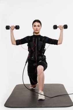 Beyaz arka plandaki kasları canlandırmak için elektirikli impulslar kullanan EMS giysili halterli kız. Elektrik kas stimülasyonu giysisinde spor eğitimi