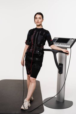 Beyaz arka planda EMS kıyafetli kız. Sağlık görevlisi kız antrenörü, acil servis giysisiyle antrenmandan önce. Elektrik kas stimülasyonu giysisinde spor eğitimi