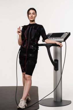 Acil servis elbiseli, elinde kontak cihazıyla beyaz arka plandaki kasları uyarmak için elektriksel dürtüler kullanan formda bir kız. Elektrik kas stimülasyonu giysisinde spor eğitimi