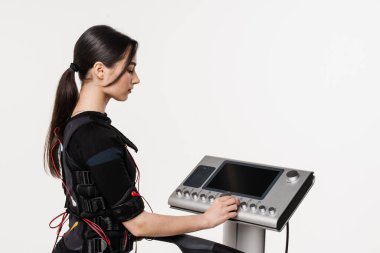 Antrenör kız, eğitimden önce EMS cihazı kuruyor. Beyaz arka planda elektriksel kas stimülasyonu giysisi spor eğitimi için EMS cihazı kur