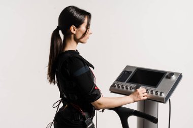 Beyaz arka planda elektriksel kas stimülasyonu kıyafeti spor eğitimi için EMS cihazı kurun. Kız çalıştırıcı eğitimden önce EMS aygıtı kuruyor