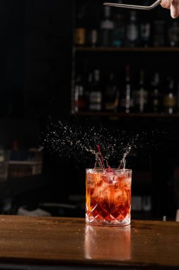Kiraz düşmesi ve Negroni 'nin alkollü kokteyline sıçraması. Barmen barda Negroni kokteyli hazırlıyor.