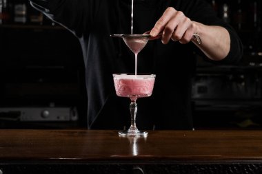 Barmen bardağa pembe Clover kulübü alkollü kokteyli döküyor. Barmen yumurta beyazı, limon, kuru vermut ve Clover Kulübü kokteylini hazırlamak için cin karıştırıyor.