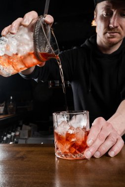 Barmen bardaki bardağa geleneksel Negroni kokteyli doldurur. Barmen cin, campari ve tatlı vermutu karıştırarak Negroni alkollü kokteylini hazırlar.