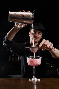 Barmen bardağa pembe Clover kulübü alkollü kokteyli döküyor. Barmen yumurta beyazı, limon, kuru vermut ve Clover Kulübü kokteylini hazırlamak için cin karıştırıyor.