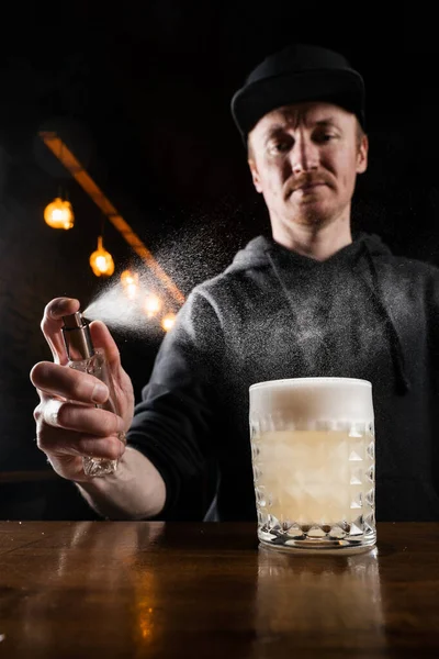 stock image Bartender is spraying whiskey over Penicillin cocktail in the bar. Bartender mixes whiskey, lemon juice, and honey-ginger syrup to prepare the Penicillin alcoholic cocktail