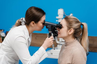 Optometrist göz doktoruna optalmoskop kullanarak bakar. Oftalmoskopi. Oftalmolog, göz doktoru olan bir kadının gözlerini inceliyor. Klinikteki bir optometriste danışmanlık